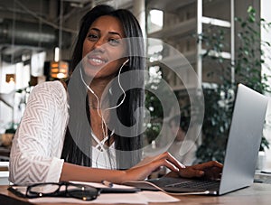 Lifestyle and people concept: portrait of happy young african woman in a coffee shop using mobile phone and laptop