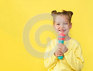 Lifestyle and people concept: a small, happy girl singing with a microphone, isolated by a bright yellow background.