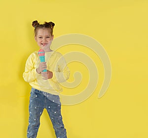 Lifestyle and people concept: a small, happy girl singing with a microphone, isolated by a bright yellow background.