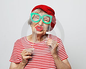 Lifestyle, people and party concept: funny grandmother wearing red clothes holding falce glasses