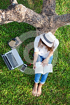 Lifestyle person Girl enjoy listening music and reading a book and play laptop on the grass field of the nature park in the mornin photo