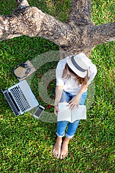 Lifestyle person Girl enjoy listening music and reading a book and play laptop on the grass field of the nature park in the mornin