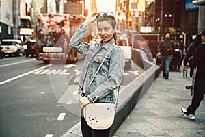 Lifestyle photo of happy young tourist adult woman looking at camera holding bag purse and sunglasses on sunny busy city street photo