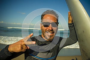 Lifestyle portrait of attractive and happy surfer man 3os to 40s in neoprene surfing swimsuit posing with surf board on the beach