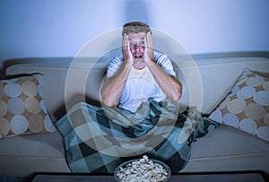 Lifestyle portrait of attractive scared and nervous man watching suspense horror movie on television feeling stressed covering wit