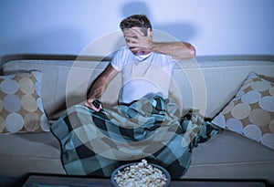 Lifestyle portrait of attractive scared and nervous man watching suspense horror movie on television feeling stressed covering wit