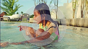 Lifestyle portrait of beautiful excited and happy child in cute girl swimsuit smiling cheerful playing with water in swimming pool