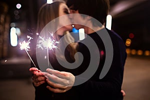 Lifestyle portrait of couple in love holding sparkling New Year fireworks on the city streets with lot of lights on background.