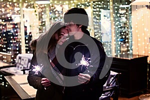 Lifestyle portrait of couple in love holding sparkling New Year fireworks on the city streets with lot of lights on background.