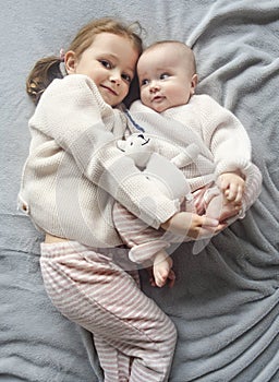 Lifestyle portrait of cute Caucasian girls sisters holding little baby on bed