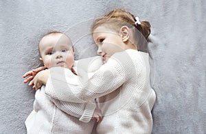 Lifestyle portrait of cute Caucasian girls sisters holding little baby on bed