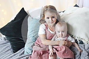 Lifestyle portrait of cute Caucasian girls sisters holding little baby on bed