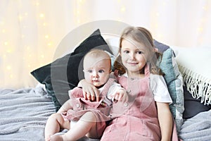 Lifestyle portrait of cute Caucasian girls sisters holding little baby on bed