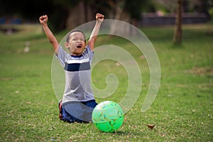Lifestyle portrait at grass city park of 5 years old Asian kid playing football happy and excited raising arms celebrating scoring