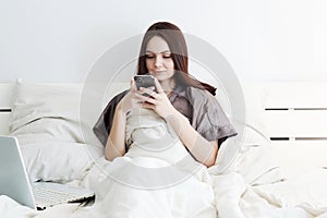 Lifestyle portrait of happy girl on bed, with laptop and smartphone