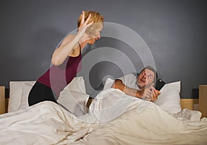 Lifestyle portrait of husband or boyfriend using mobile phone in bed with angry frustrated wife or girlfriend feeling ignored and