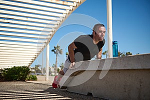 Lifestyle portrait of a male athlete doing exercises on arms and back muscles, pushing up during bodyweight training