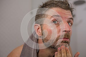 Lifestyle portrait of mid adult attractive concerned and upset man at home bathroom looking at the mirror grey hair on his beard