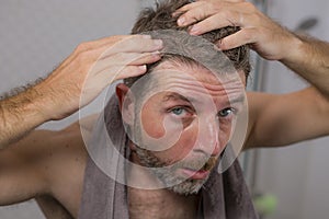 Lifestyle portrait of mid adult attractive concerned and upset man at home bathroom searching and finding gray hair looking at the