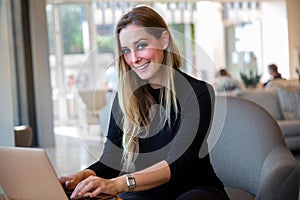 Lifestyle portrait of a modern business woman entrepreneur, sitting with laptop in a bright workspace, smiling and cheerful.