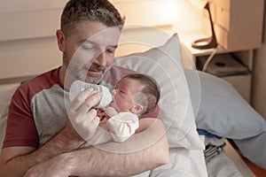 Lifestyle portrait of proud happy man holding tenderly bottle feeding her child - an adorable and beautiful newborn baby girl in