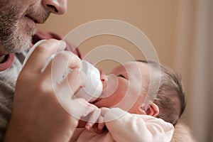 Lifestyle portrait of proud happy man holding tenderly bottle feeding her child - an adorable and beautiful newborn baby girl in