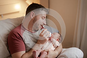 Lifestyle portrait of proud happy man holding tenderly bottle feeding her child - an adorable and beautiful newborn baby girl in