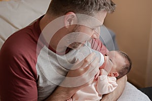 Lifestyle portrait of proud happy man holding tenderly bottle feeding her child - an adorable and beautiful newborn baby girl in