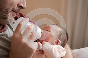 Lifestyle portrait of proud happy man holding tenderly bottle feeding her child - an adorable and beautiful newborn baby girl in