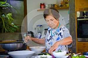 Lifestyle portrait of senior happy and sweet Asian Japanese retired woman cooking at home kitchen alone neat