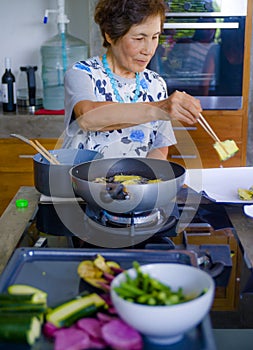 Lifestyle portrait of senior happy and sweet Asian Japanese retired woman cooking at home kitchen alone neat and tidy