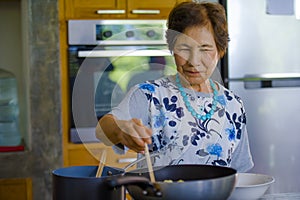 Lifestyle portrait of senior happy and sweet Asian Japanese retired woman cooking at home kitchen alone neat and tidy photo