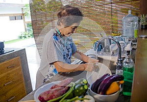 Lifestyle portrait of senior happy and sweet Asian Japanese retired, woman cooking at home kitchen washing the dishes