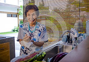 lifestyle portrait of senior happy and sweet Asian Japanese retired, woman cooking at home kitchen washing the dishes