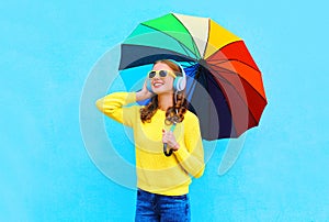 Lifestyle portrait smiling young woman listens to music in headphones with colorful umbrella in autumn day over colorful blue