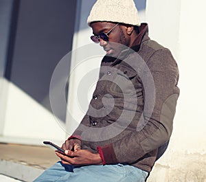 Lifestyle portrait of stylish young african man using smartphone in city