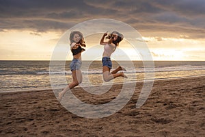 Lifestyle portrait of two happy and attractive young Asian Korean women girlfriends jumping on sunset beach excited and cheerful e