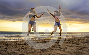 Lifestyle portrait of two happy and attractive young Asian Korean women girlfriends jumping on sunset beach excited and cheerful e