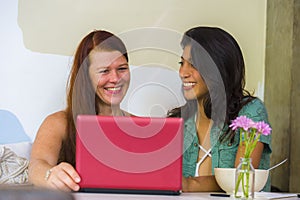 Young happy and beautiful caucasian and hispanic women working at office cafe with laptop computer as digital business partners