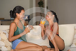 Lifestyle portrait of two young happy and relaxed Asian girlfriends having fun talking laughing and gossiping at home sofa couch s