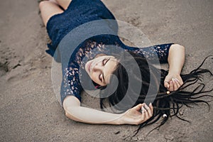 Lifestyle portrait of a woman brunette on background of the lake lying in sand on a cloudy day. Romantic, gentle, mystical