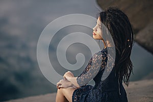 Lifestyle portrait of a woman brunettes in background of lake sitting in sand on a cloudy day. Romantic, gentle, mystical