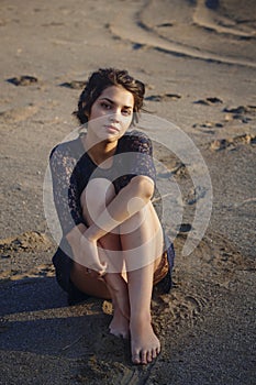 Lifestyle portrait of a woman brunettes in background of lake sitting in sand on a cloudy day. Romantic, gentle, mystical