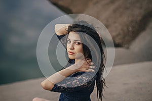 Lifestyle portrait of a woman brunettes in background of lake sitting in sand on a cloudy day. Romantic, gentle, mystical