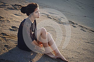 Lifestyle portrait of a woman brunettes in background of lake sitting in sand on a cloudy day. Romantic, gentle, mystical