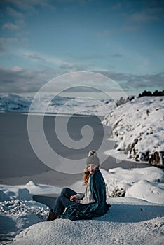 Lifestyle portrait of woman cuddled up in blanket posing in snow on an amazing sunny winter day in Scandinavia.