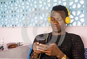 Lifestyle portrait of young attractive and cool hipster black afro American man using mobile phone and headset networking on