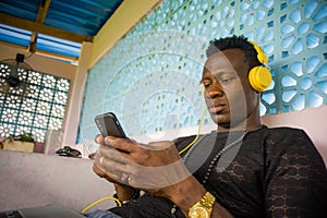 Lifestyle portrait of young attractive and cool hipster black afro American man using mobile phone and headset networking on
