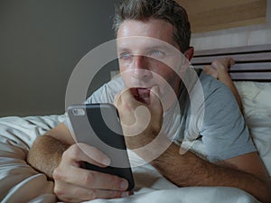 Lifestyle portrait of young attractive and relaxed man at home bedroom using mobile phone lying on bed thinking and daydreaming