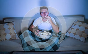 Lifestyle portrait of young attractive relaxed man watching movie on television eating popcorn sitting late night at living room s